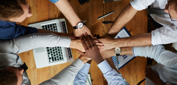 Symbolbild: Teammitglieder legen über einem Schreibtisch die Hände zusammen